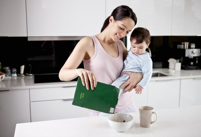 Young mother holding her baby son whilst making breakfast