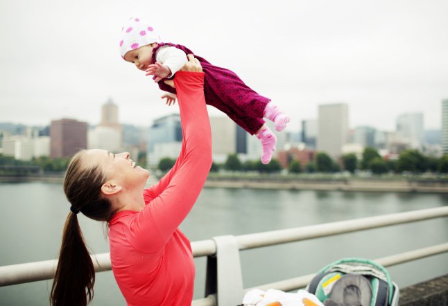 Running mom playfully lifting baby up on city bridge