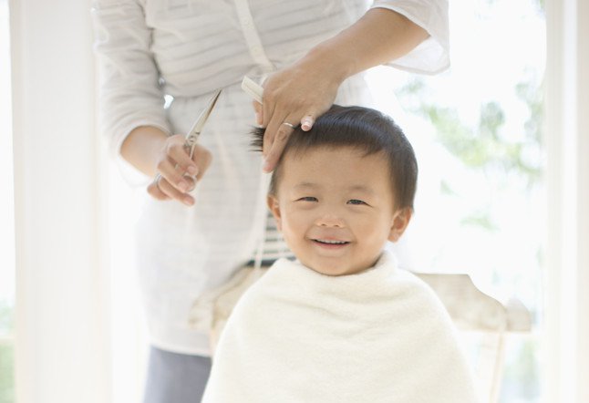 Baby boy having hair cut by mother