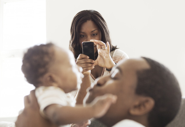Mother taking photo of father playing with baby son (2-5 months)