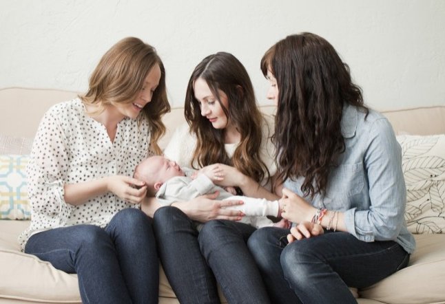 USA, Utah, Salt Lake City, Three young female friends sitting on sofa with baby boy (2-5 months) o0n their lap