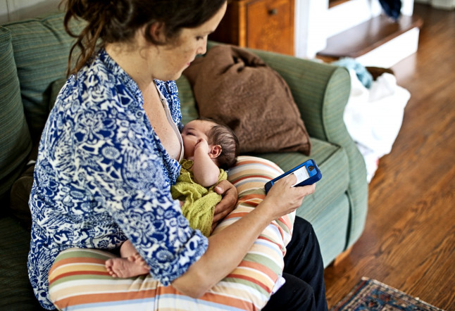 Mother breast feeding newborn baby boy while texting on her iphone.