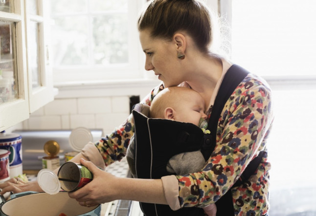 Mid adult mother with baby son in sling preparing food in kitchen