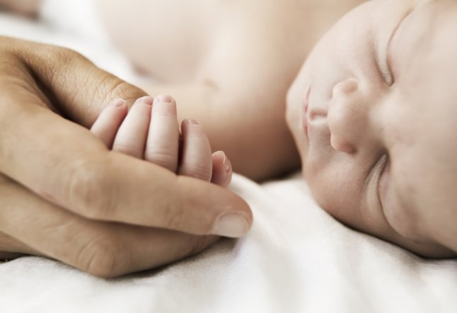 Mother holding hand of her sleeping newborn son