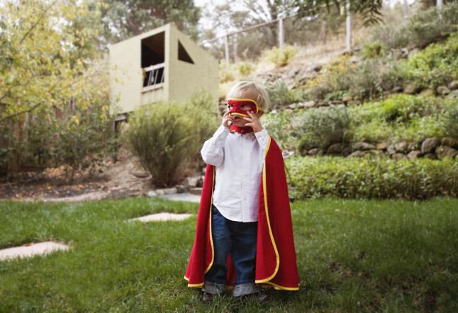 Boy wearing cape and mask in backyard